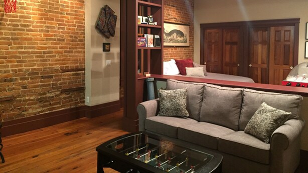 A living room with a brick wall, a sofa, a coffee table, a bookshelf, and a door.