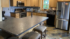 Cozinha moderna com armários de madeira, uma ilha grande com banquetas, eletrodomésticos de aço inoxidável e uma janela com vista.