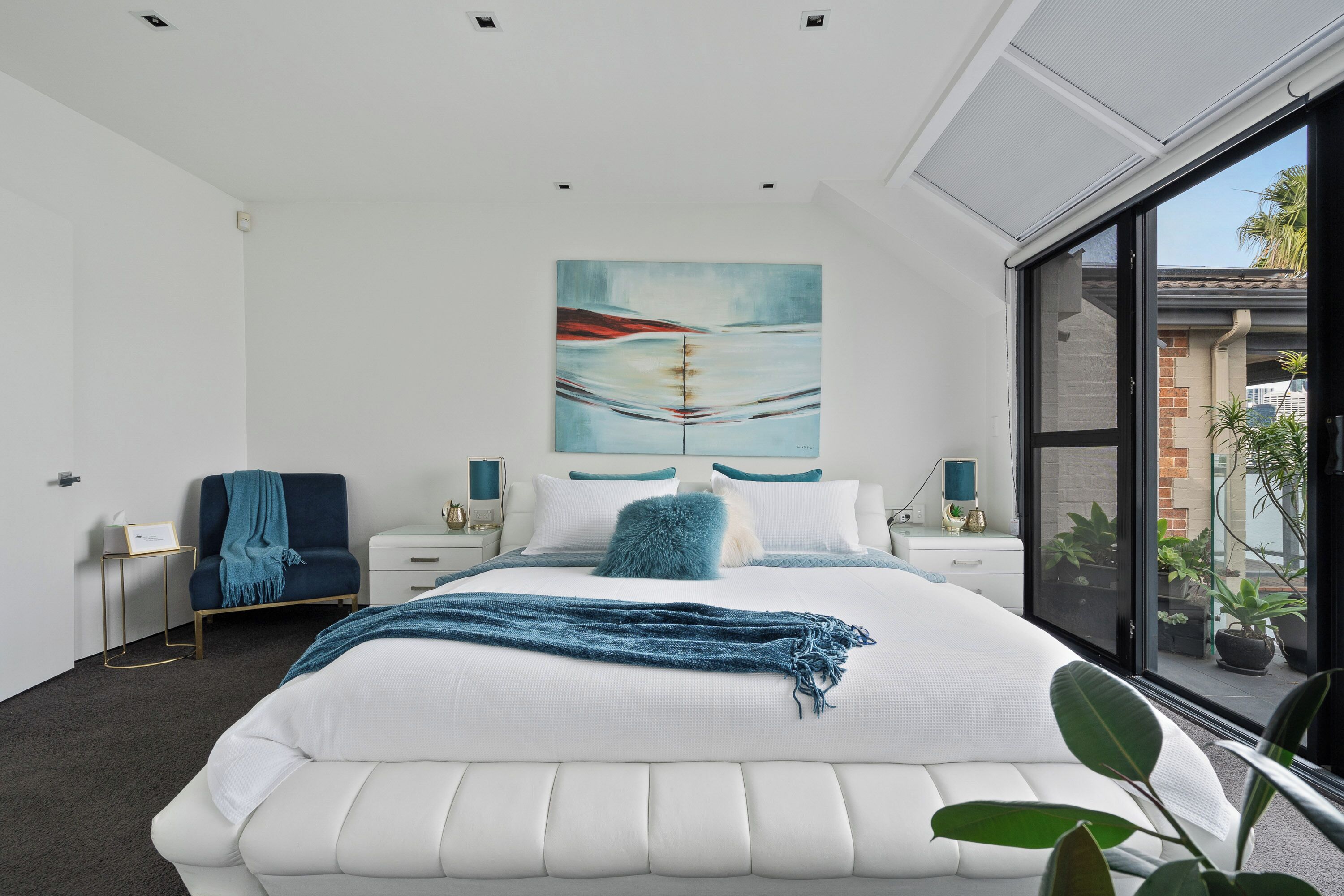 Un dormitorio moderno con una cama grande, un cuadro en la pared y vistas al exterior a través de un amplio ventanal.