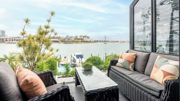 Un balcón con mobiliario de mimbre, una mesa de vidrio y vistas a un puerto deportivo y el horizonte de la ciudad.