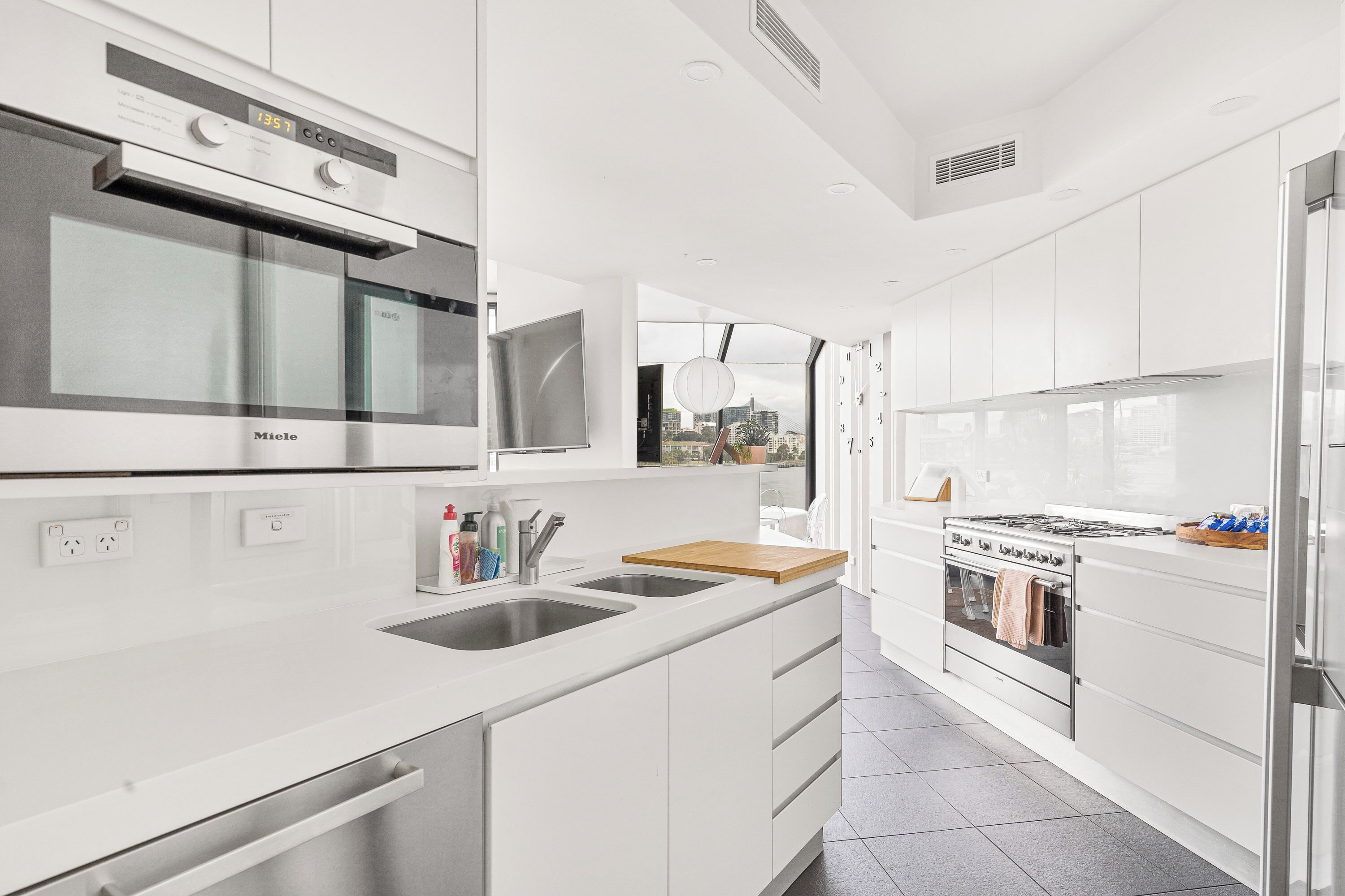 A modern kitchen with white cabinetry, stainless steel appliances, and a large window offering a city view.