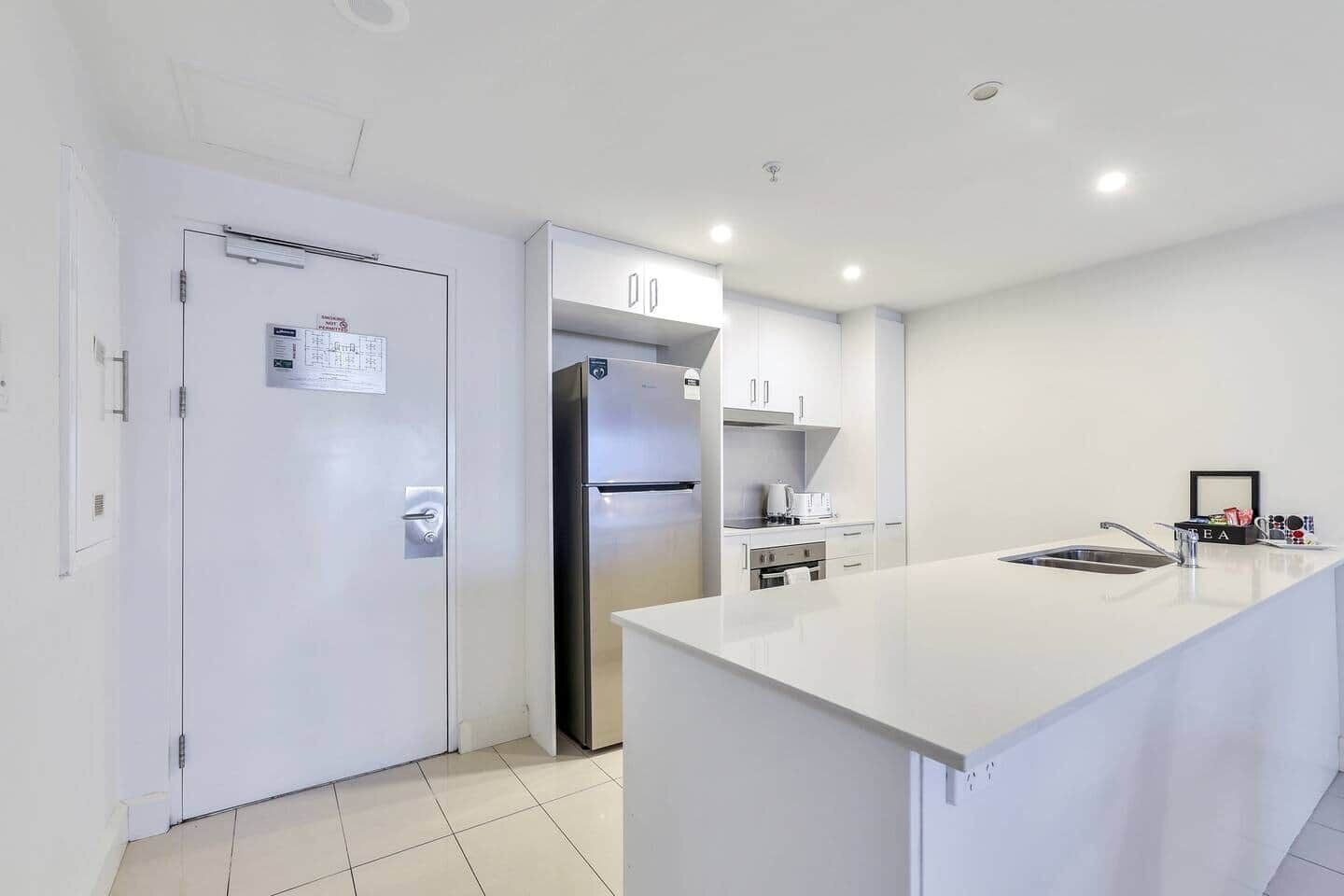 A modern kitchen with white cabinetry, a stainless steel refrigerator, and a white countertop.