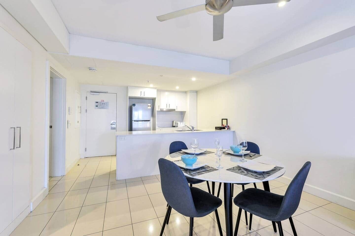 A modern kitchen with a refrigerator, stove, and sink. There is a dining area with a table set for two and two chairs.