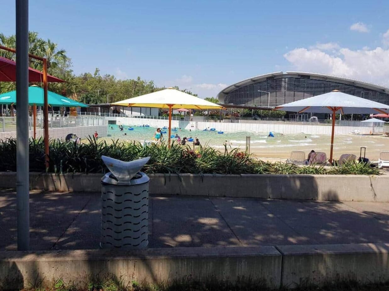 A beach area with umbrellas, a trash bin, and a large building in the background.