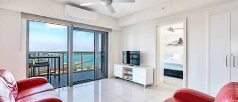 Una sala moderna con balcón, televisor y cama en la habitación contigua.