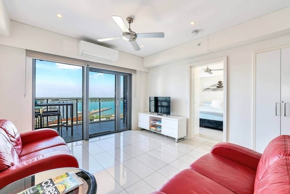 A modern living room with a balcony, a TV, and a bed in the adjacent room.