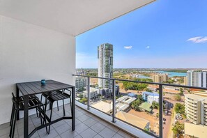 A balcony with a table and chairs, overlooking a cityscape with high-rise buildings and a body of water.