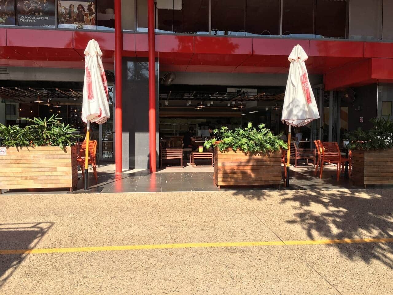 An outdoor seating area with tables and chairs, a red building facade, and potted plants.