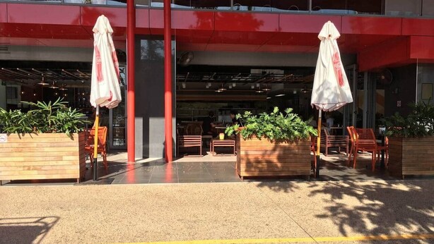An outdoor seating area with tables and chairs, a red building facade, and potted plants. - Darwin City Harbour Views-above the Oak Restaurant (Darwin City)