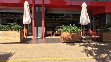An outdoor seating area with tables and chairs, a red building facade, and potted plants.