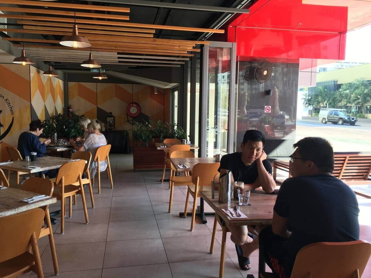 An indoor dining area with wooden tables and chairs, a red awning, and a view of the street outside.