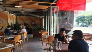 An indoor dining area with wooden tables and chairs, a red awning, and a view of the street outside. - Darwin City Harbour Views-above the Oak Restaurant (Darwin City)