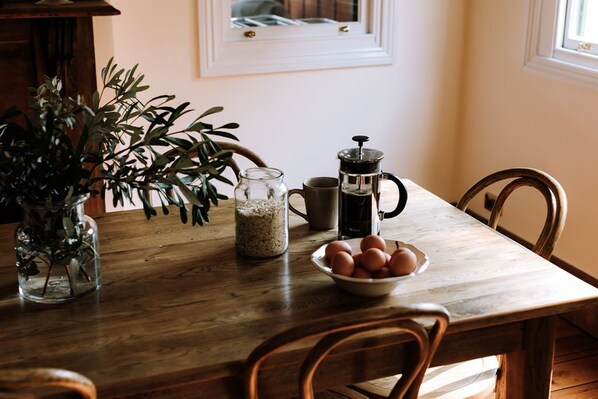 A wooden dining table with a coffee maker, a bowl of eggs, and a jar of grains.