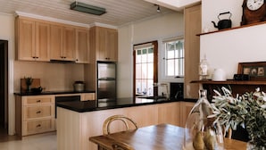 Uma cozinha com armários de madeira, geladeira de aço inoxidável, bancada preta e mesa de jantar com cadeiras.