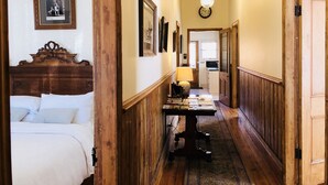 Un couloir avec un plafond en bois, des tableaux encadrés accrochés aux murs, un lit sur la gauche et une table sur laquelle sont posés divers objets.
