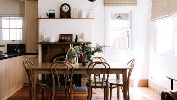 Uma sala de jantar com mesa e cadeiras de madeira, lareira e janela com cortinas.