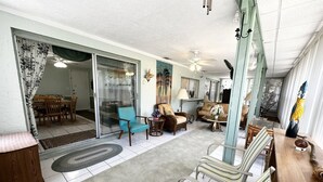 Un salón amplio con comedor, puertas de vidrio correderas y diversas opciones de asientos, incluyendo un sofá, sillones y una silla a rayas.