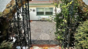 Un arco de piedra que conduce a una casa de paredes blancas y ventana verde.