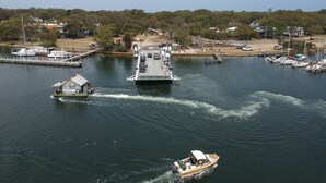 A ferry dock with a large ferry and smaller boats, surrounded by a calm water body and a distant shoreline with buildings and trees.
