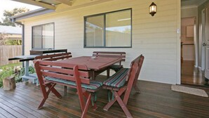 An outdoor patio with a wooden table and benches, a window, and a door. - Bring the Dog, Bring the Boat, Bring the Family (Burrill Lake)