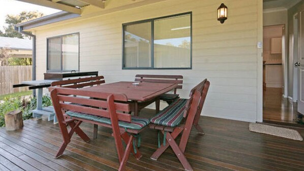An outdoor patio with a wooden table and benches, a window, and a door.