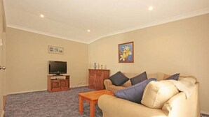 A living room with a beige sofa, a wooden coffee table, a television on a stand, and a cabinet. - Bring the Dog, Bring the Boat, Bring the Family (Burrill Lake)