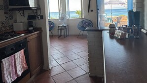 A kitchen with a view of the sea, a dining area with chairs, and a counter with items on it. - Casa delle Galee - Garden on the Sea  (Scilla)