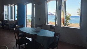 An open-plan living area with a dining table, chairs, and large windows overlooking the sea. - Casa delle Galee - Garden on the Sea  (Scilla)