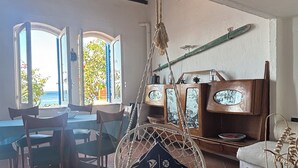 A room with a hanging chair, a table with magazines, and a view of the sea through large windows. - Casa delle Galee - Garden on the Sea  (Scilla)