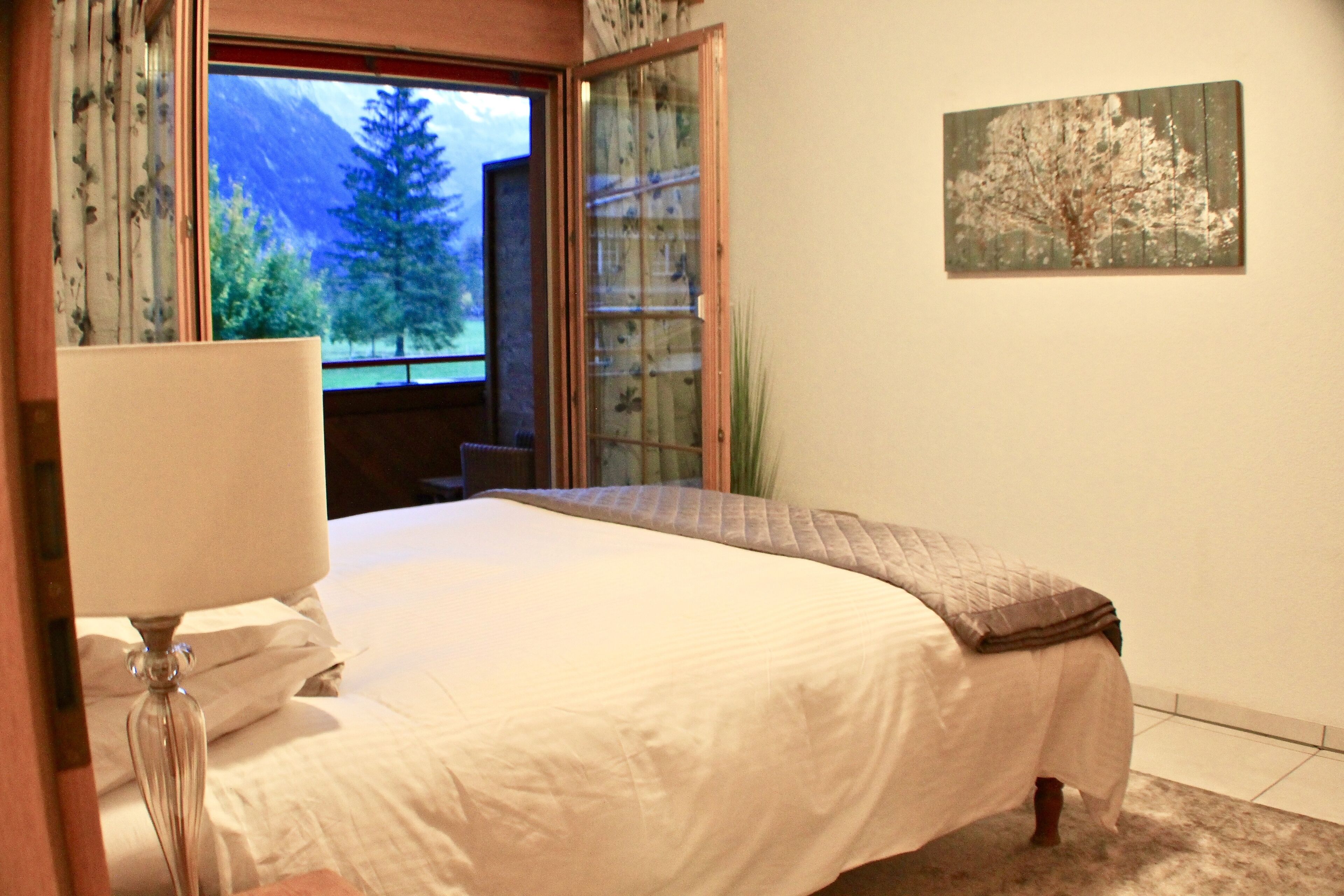 Ein Schlafzimmer mit einem Bett, einem Fenster mit Blick auf Bäume und einem Bild an der Wand.