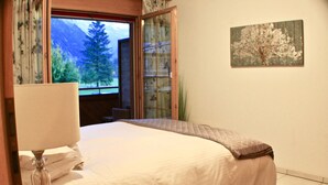 A bedroom with a bed, a window with a view of trees, and a painting on the wall.