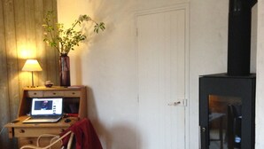 A room with a wooden desk, a laptop, a vase with flowers, a black cabinet, and a dining table with chairs.