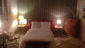 A hotel room with a bed, a wooden dresser, a desk with a lamp, and a chair.