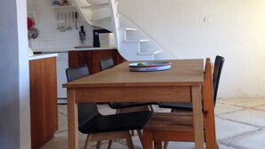 A dining area with a wooden table and chairs, a kitchen in the background, and a white staircase.