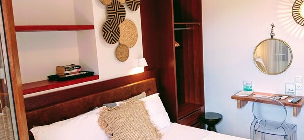 A hotel room with a bed, a bedside table with a lamp, a mirror, a shelf with books, a wall-mounted decorative item, and a small desk with a phone and a sign indicating free Wi-Fi. - EUROPA,2BR,2BTH VILLA WITH PRIVATE POOL AND STUNNING SEA VIEWS (SKIATHOS)