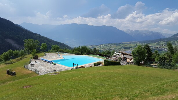 A swimming pool with a stone deck, surrounded by a grassy area and a view of mountains. - STUDIO 17m², 5 BEDS (Les Orres)