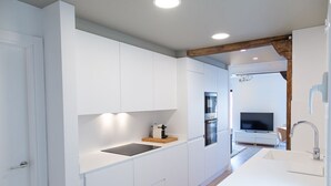 A modern kitchen with white cabinetry, a central island with a sink, and a built-in oven. - SAN SEBASTIAN TRAIN & BUS STATION TOURIST FLAT (DONOSTIA)