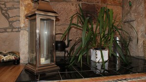 A room with a stone wall, a black tiled floor, a wooden table, a glass lantern, a potted plant, and a metal teapot. - Beautiful cottage by the sea. (Nairn)