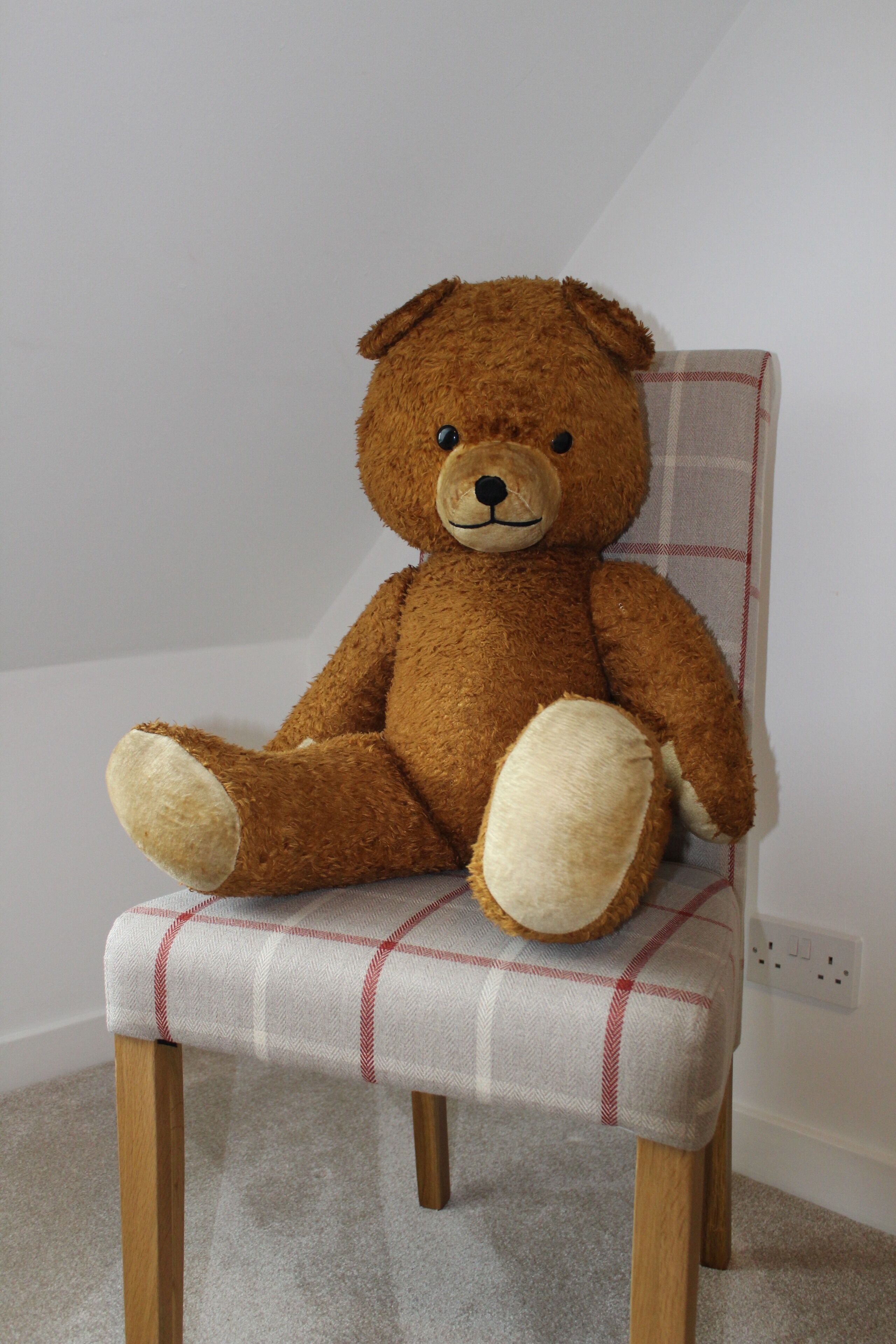 En brun bamse sidder på en ternet stol med træben.