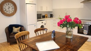 A modern kitchen with white cabinets, a wooden dining table, and a vase of roses. - Beautiful cottage by the sea. (Nairn)