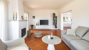 A modern living room with a fireplace, a grey sofa, a round coffee table, and a TV. - Villa Atlantico (Carvoeiro)