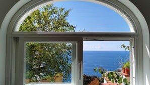 Une fenêtre offrant une vue dégagée sur la mer et un balcon agrémenté de plantes en pot.