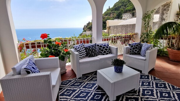 Un balcon agrémenté de meubles en osier peints en blanc, d’un tapis à motifs et de plantes en pot.