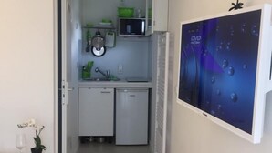 A narrow hallway leading to a compact kitchen with white cabinets, a microwave, and a small refrigerator. A flat-screen TV is mounted on the wall to the right. - W-Lan, kitchenette, bathroom, shower, sofa bed, smart TV (Leverkusen - Hitdorf)