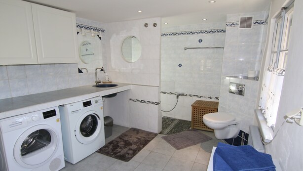 Ein kleines Badezimmer im Hotel mit Waschmaschine, Toilette, Duschbereich und Handtuchhalter.