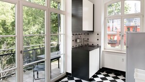 A modern kitchen with large windows, a black and white checkered floor, and a view of a red building outside. - LE Home II: 2-room loft w/ balcony+parking. Quiete, bright! (Plagwitz)