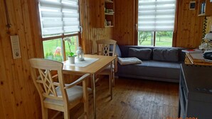 A wooden cabin interior with a dining table, two chairs, a sofa, and a window with blinds. - Harz vacation under the apple tree  (Cattenstedt)