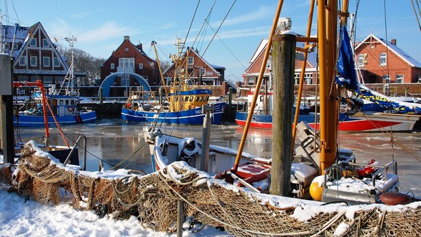 A harbor with boats docked, wooden buildings, and fishing nets on the ground. - Last-Minute Summer Deals! A vacation right on the beach! (Neuharlingersiel)