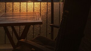 A sunset view from a balcony with a wooden table and chairs, overlooking a body of water and buildings. - Last-Minute Summer Deals! A vacation right on the beach! (Neuharlingersiel)