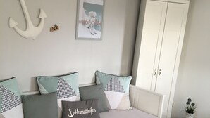 A bedroom with a bed, pillows, a wardrobe, a small table with a plant, and wall decorations including an anchor and a framed picture. - Last-Minute Summer Deals! A vacation right on the beach! (Neuharlingersiel)